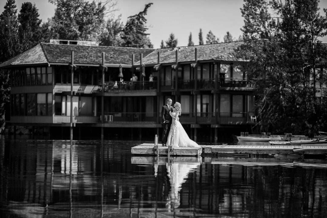 Elegant wedding couple on dock by water with modern Canmore Banff Calgary wedding photographers, capturing romantic moments in scenic Mountain Alberta setting.