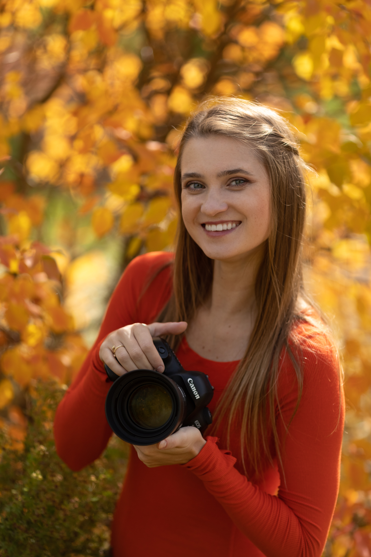 Vibrant autumn portrait of a female photographer holding a Canon camera outdoors in Canmore Banff, highlighting professional wedding and portrait photography services.
